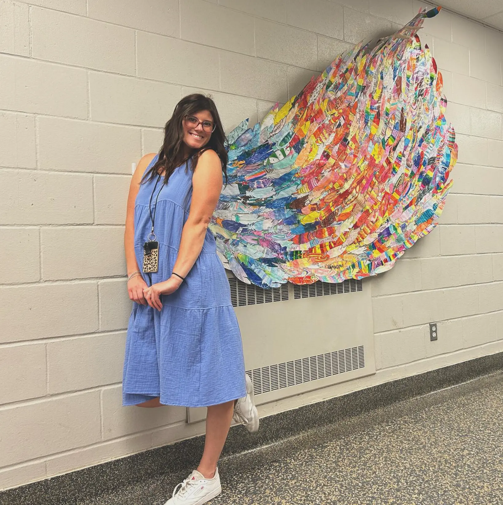 HARVYN's founder, a teacher, standing beside a colourful student-made wing mural in a school hallway
